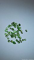 Multiple small green tsavorite garnet gemstones scattered on a plain light surface, showcasing their color and cuts.