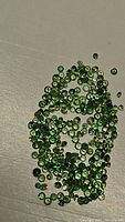 Photo showing a collection of small round diamond cut natural tsavorite garnet gemstones, bright apple green in color on a plain surface.