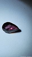 Close-up image of a pear-shaped faceted sapphire showing deep purple fuchsia color in direct light.
