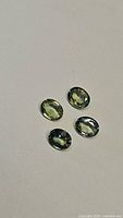 Four natural oval cut sapphires in green, yellow, and blue tones on a white background, showing color variations and faceting details.