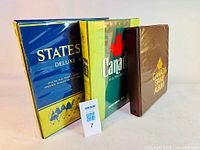 Three stamp albums including a blue and yellow deluxe States album, a green Canadian album, and a brown Canada album.