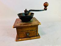 Full view of antique coffee grinder showing wooden base, cast iron bowl, and curved metal handle with wooden knob.