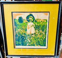 Framed art print showing a child wearing a hat in a flower field. Yellow matting and black frame visible.
