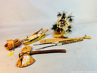 Miniature birch bark basket, canoe, wooden tomahawk, spear, paddle, and corn husk kachina doll arranged on flat surface.