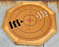 Octagonal crokinole board setup with black and natural wood discs arranged on the cork playing surface marked with scoring rings.