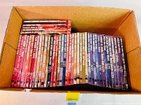 Top-down view of all 34 books laid flat in a cardboard box with colorful spines predominantly red and blue, titles clearly visible.