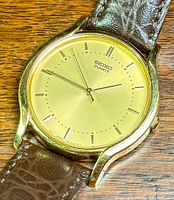 Close-up photo of gold tone SEIKO quartz watch face with gold markers and hands.