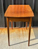 Front three-quarter view of walnut side table showing drawer and tapered legs