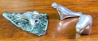 Three polished stainless steel animal figurines on a wood surface, including one seal mounted on green stone base.