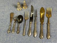 Photo showing multiple sterling silver tableware pieces including forks, knives, salt and pepper shakers, a large spoon, and spreader.