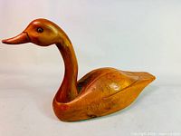 Side view of full wooden goose sculpture showing body with carved feather details and long neck with varnished surface.
