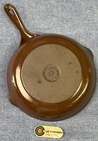 Cast iron skillet bottom showing Le Creuset embossed logo, size 23, and French origin stamp, with original Le Creuset sticker placed next to skillet.