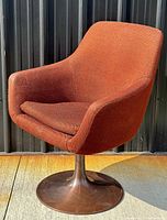 Angled side view of vintage mid century modern tulip chair showing orange fabric upholstery and bronze metal round base with scratches