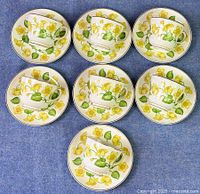 All seven tea cups paired with saucers arranged on blue surface