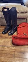 Pair of black riding boots standing with red boot bag nearby