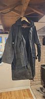 Front view of full-length black waxed cotton trench coat on hanger