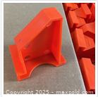 Close-up of one orange flooring spacer showing its angular design and two holes for positioning on the floor edge.