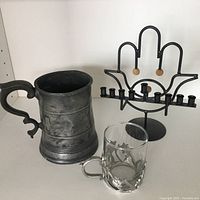 Pewter half pint tankard, glass tea holder cup, and metal Hanukkah menorah arranged together on white surface.