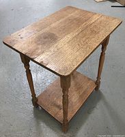 Side view of antique wood side table showing the turned carved legs and lower shelf.