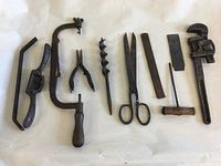 Full view of 10 antique and vintage tools laid on white background, showing variety of saws, wrench, shears, and bits.