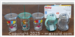 Five Nuby baby and kids' cups including two trainer cups and three swirly straw tumblers arranged on a table.
