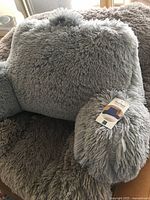 Gray plush backrest pillow with arms placed on a plush shaggy blanket, showing the texture and size of the pillow
