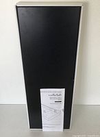 Front view of the boxed black floating shelf showing label details.