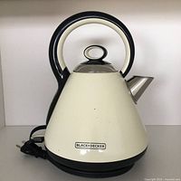 Cream-colored BLACK+DECKER cordless electric kettle with black handle, base, and lid top, front view showing brand logo.