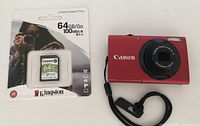 Packaged 64 GB Kingston Canvas Select Plus SD card alongside red Canon camera body and wrist strap.