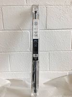 Full packaged curtain rod, shrink-wrapped in plastic with label "Curtain Rod Triangle a rideau" and sizing details 28-48 inch adjustable.
