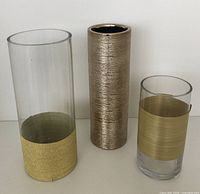 Front view of three cylinder vases: one gold textured vase, two clear glass vases with gold bands.