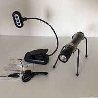 Photo showing the rechargeable clip-on book light with flexible neck, clip base, USB charging cable, user manual, and the Nite Ize Flashlite Friend attached to a Mini MagLite.
