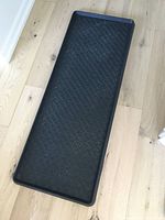 Top-down view of rectangular black boot tray with raised edges placed on wooden flooring.