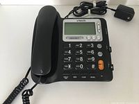 Front of black VTech Big Button corded telephone with numeric keypad, emergency button, and LCD display for caller ID. Includes handset, coiled cord, and power adapter.