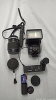 Photo showing the full lot spread: Vivitar flash, Olympus Winder 2 motor drive, Olympus 135mm f/2.8 lens, lens cap, lens cleaner blower brush, film canister, and camera strap.