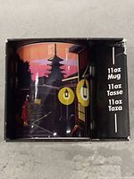 Front view of the Godzilla mug inside its factory box showing part of the cityscape design and packaging text indicating 11oz size.