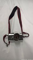 Front view of Olympus OM-2 camera with attached fabric strap on white background.
