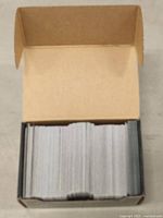 Top-down view of a small cardboard box filled with Magic: The Gathering trading cards from above, cards mostly face down or obscured.