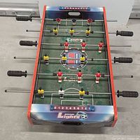 Mini foosball table front angled view showing player figures, rods, and score counters.
