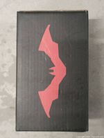 Black box with red Batman logo on one side, showing the iconic bat emblem in stylized form.