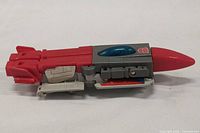 Side view of the G1 Broadside figure in jet mode showing red and gray body with blue cockpit and Autobot logo.