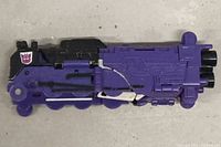 Front and side views of Transformers G1 Astrotrain figure in train mode showing purple, black, and white coloration with Decepticon logo.
