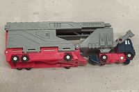 Side view of the Transformers G1 Overload figure in truck vehicle mode showing red, grey and blue colors with wheels undercarriage.