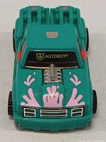 Front view of teal Autobot truck vehicle with pink splash decals showing chrome engine and Autobot logo on windshield.