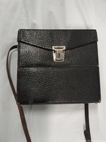 Black leather textured carrying case with a metal clasp and attached strap, closed position