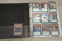 Open black 3-ring binder with Yu-Gi-Oh cards inside plastic sleeves, showing cards with fantasy artwork.