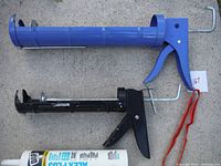 Two caulking guns laid out on concrete, blue and black, showing overall condition and design.