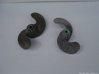 Two vintage small outboard motor propellers, showing front view, placed on white surface.
