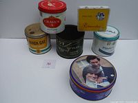 Five old tobacco tins displayed on a table with a white background. Brands visible: Craven A, Black Cat, Player's, Pitman To Plug, and Pikeur Ritmeester. One dated royal wedding tin.