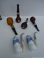 All six smoking pipes laid flat on white surface showing variety of styles including two white porcelain Meerschaum and four wooden pipes